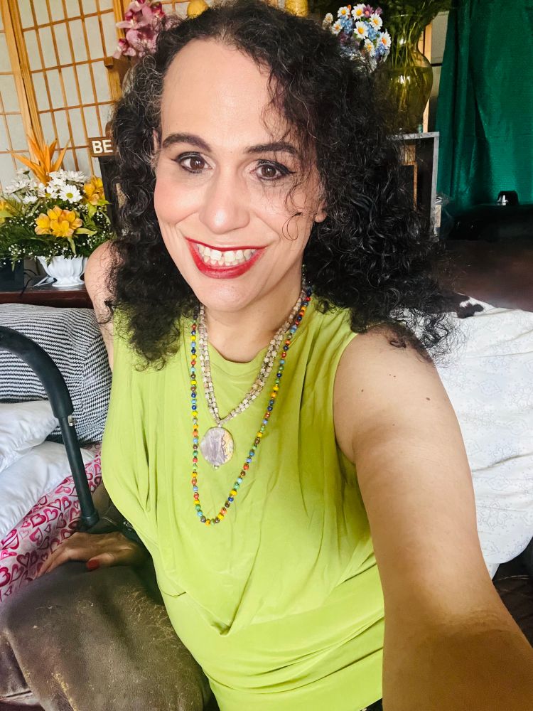 A 42 year old trans woman in a lime green tank with a rainbow necklace and a cream colored necklace.