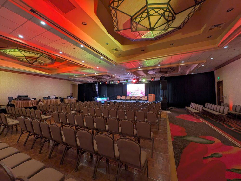 A photograph of main stage while the room was empty, in preparation for Opening Ceremonies. Striking red and yellow lights shine across the ceiling.