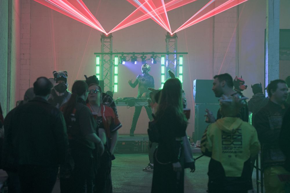 A photograph of Avian Invasion DJ'ing for a small crowd. Red lasers blast overhead.
