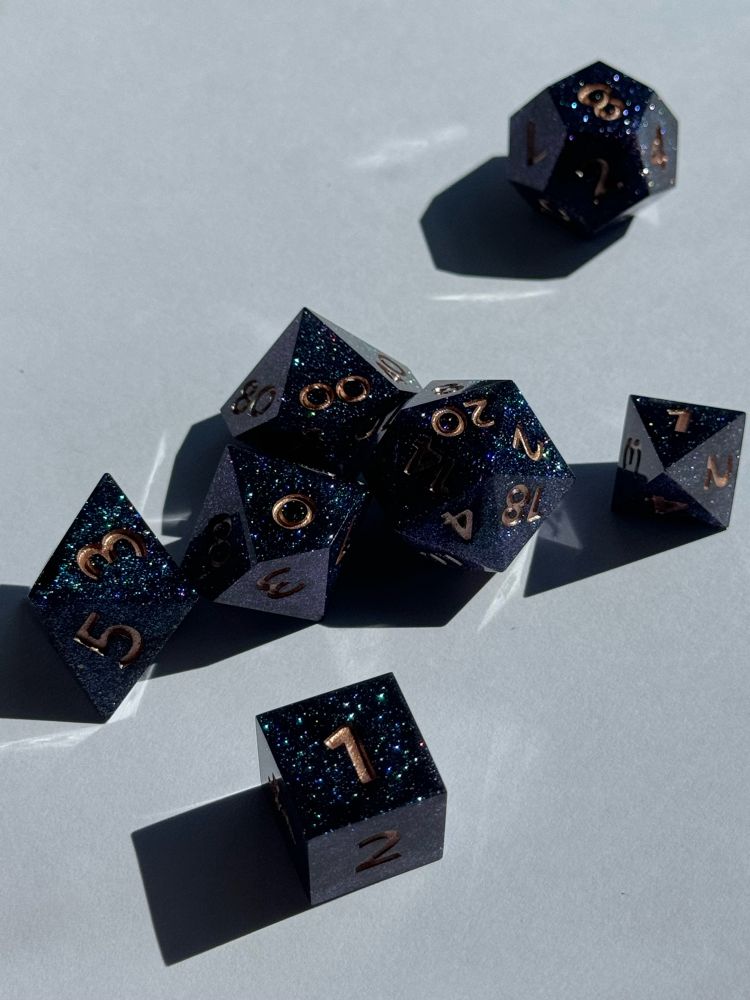 Teal/purple sparkly set of 7 assorted dice sit on a white background in the sun.