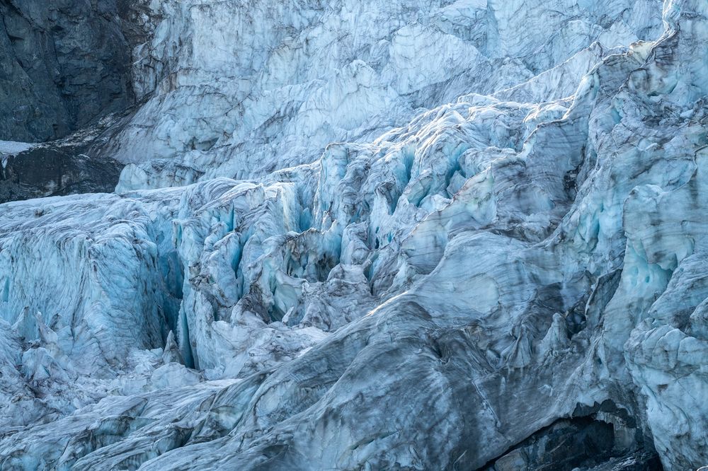 Close-up view of heavily fractured glacier ice showing intricate patterns of crevasses and seracs. The white and blue ice formations create a complex maze of ridges, valleys, and vertical walls with detailed textures and shadows throughout the icefall.