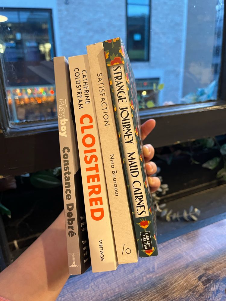 The spines of four books: Playboy by Constance Debré; Cloistered by Catherine Coldstream; Satisfaction by Nina Bouraoui; Strange Journey by Maud Cairnes