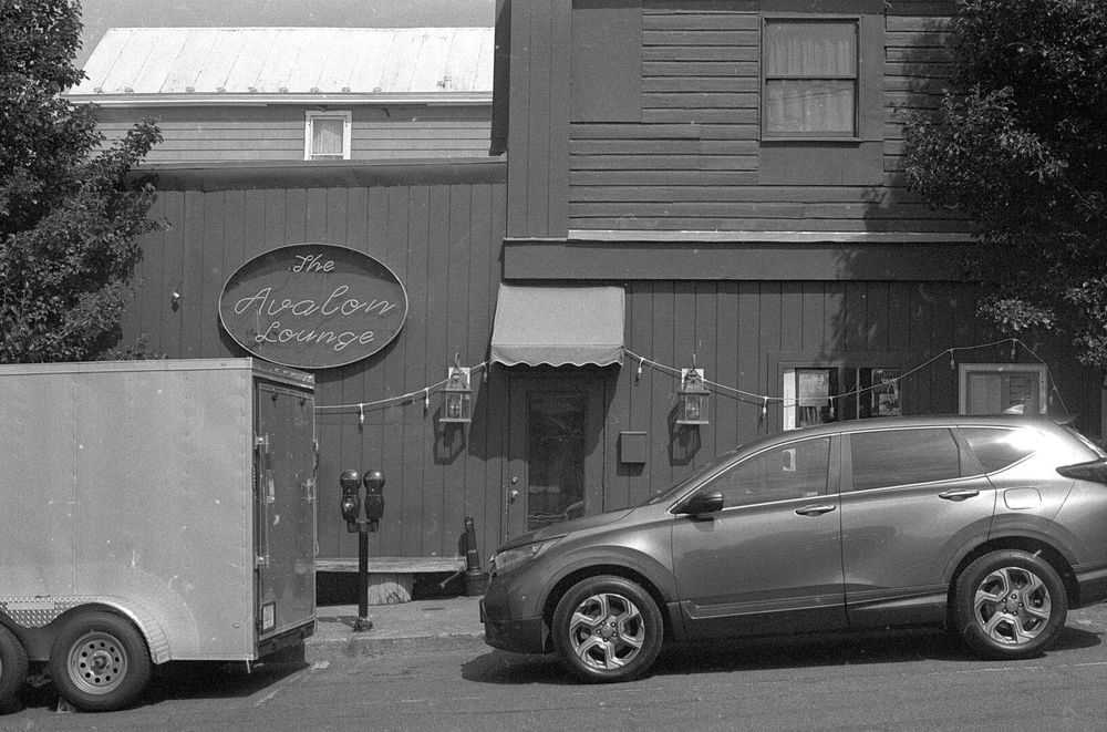 A gray building with a neon sign on it that reads “The Avalon Lounge”.