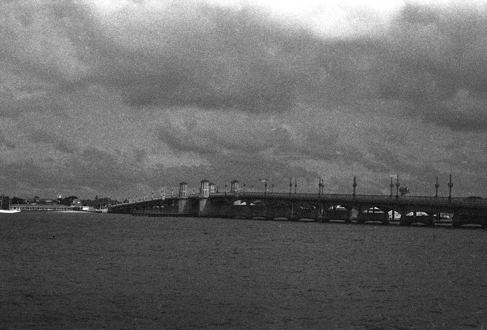 A drawbridge goes over a tidal estuary under a heavily overcast sky.