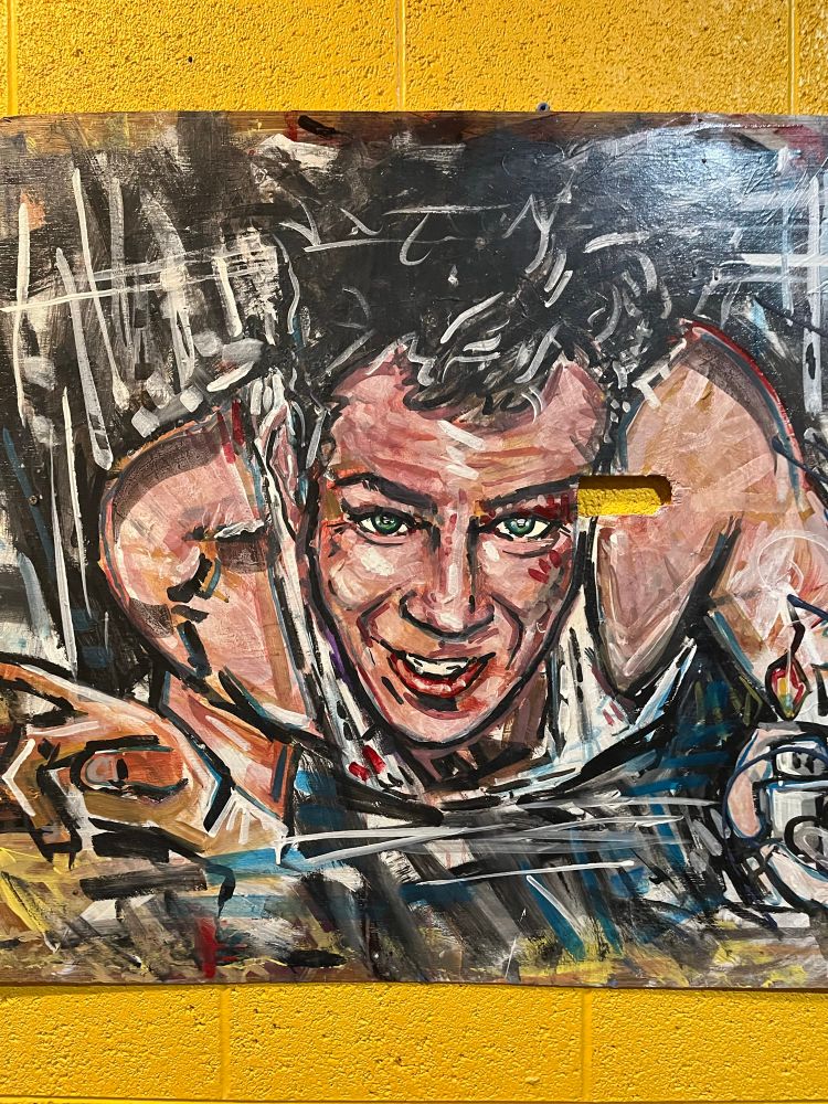 A painting of Bruce Willis as John McClane in a scene from Die Hard in which he crawls through an air duct to escape terrorists who’ve overtaken an office building. 
