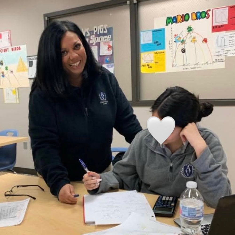 Therese smiling at the camera while assisting a student with their work in a classroom
