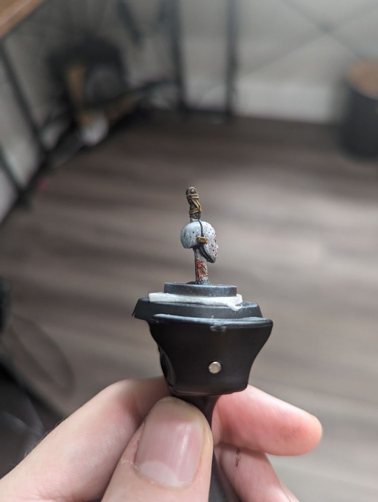 A painted miniature of a hockey mask head skewered by a sword