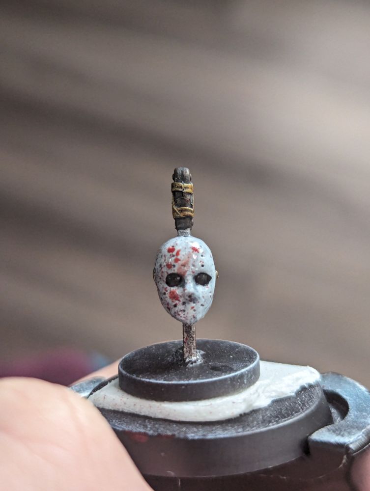 A painted miniature of a hockey mask head skewered by a sword