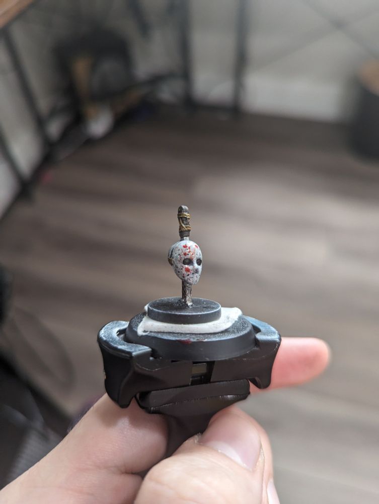 A painted miniature of a hockey mask head skewered by a sword