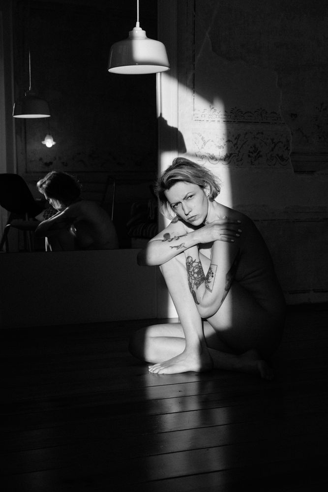 Schwarz weiß Foto. Model sitzt im Licht, welches durch die Balkontür fällt und schaut in die Kamera 