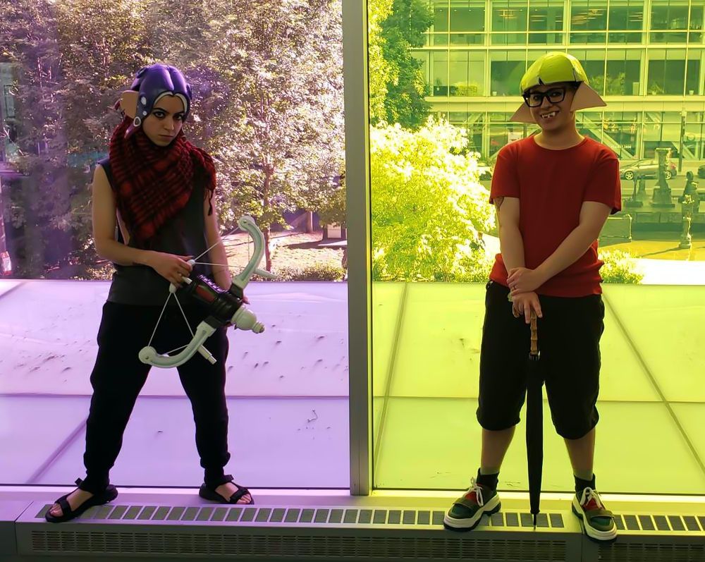 Two Splatoon cosplayers face the camera, one purple Octoling on the left with a REEF-LUX 450 for his weapon, and a green Inkling on the right with an Undercover Brella