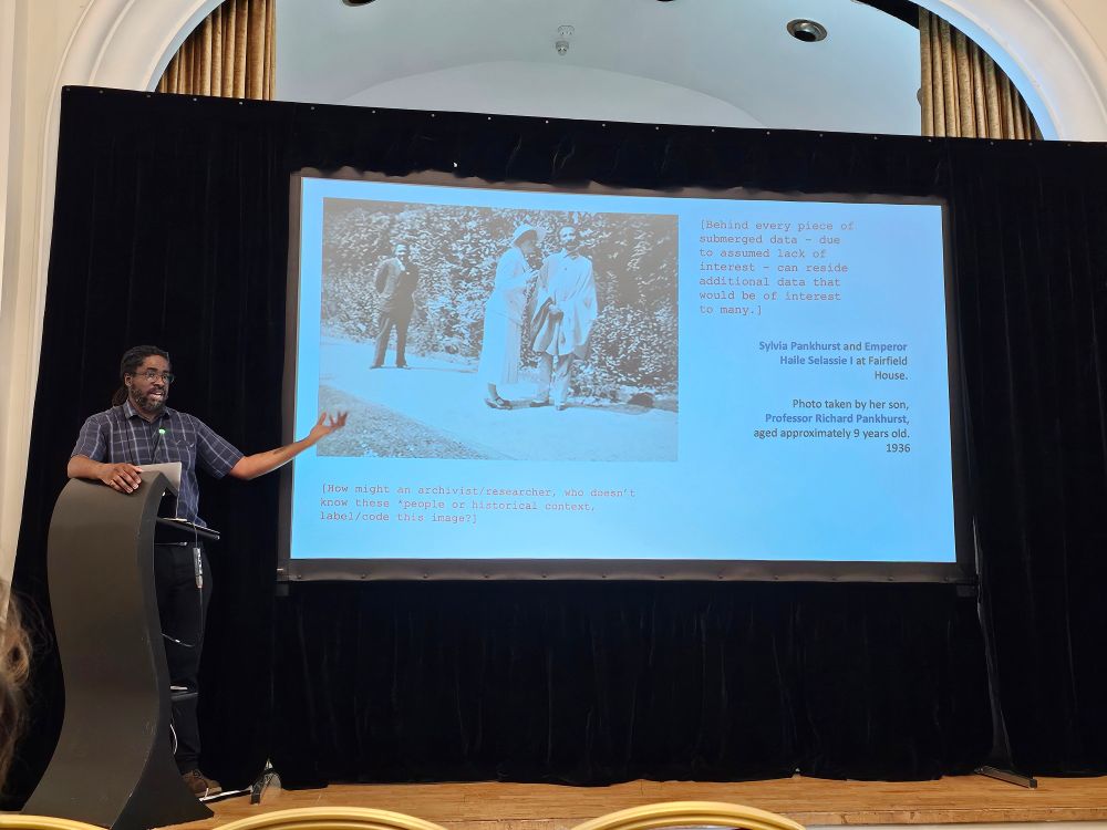 Prof Sobers presenting slides on a stage. Slides depicting Sylvia Pankhurst an Emporer Haile Selassie I 