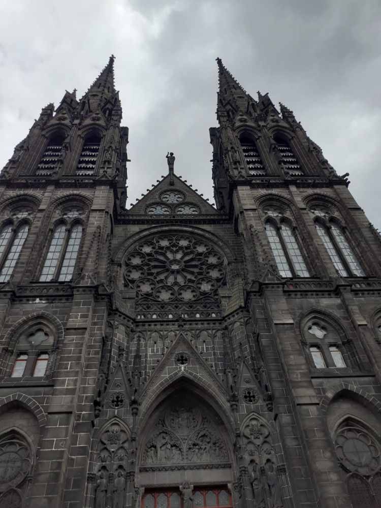 La façade de pierres noires d'une cathédrale gothique en pierres noires prise en contre-plongé, ce qui la rend très imposante