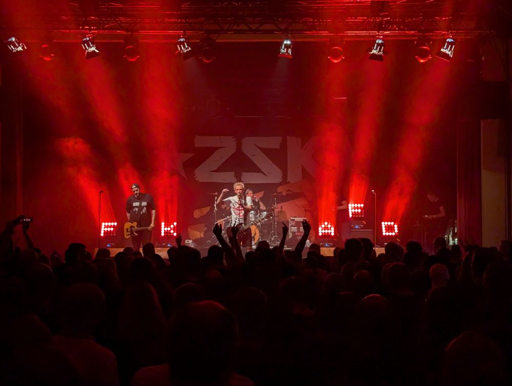 Die Band ZSK auf der Bühne im Alten Schlachthof Dresden. Die Bühnenbeleuchtung zeigt den Text "FCK AFD"