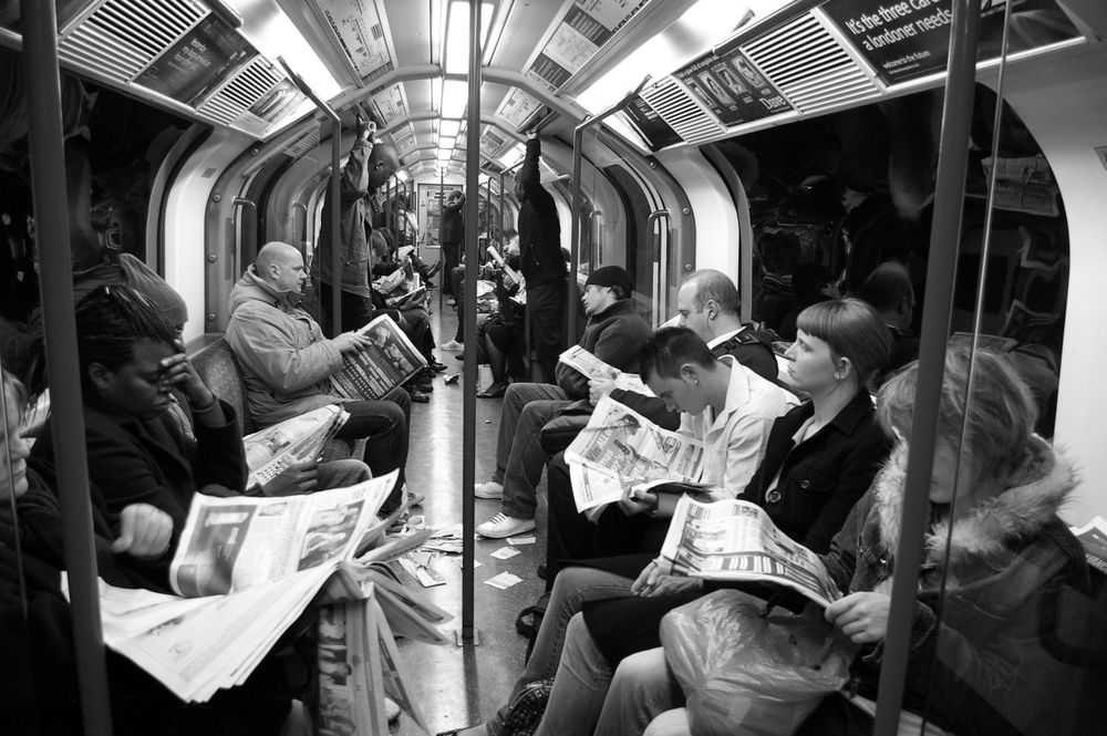 A black and white image of people in a tube carriage all reading newspapers