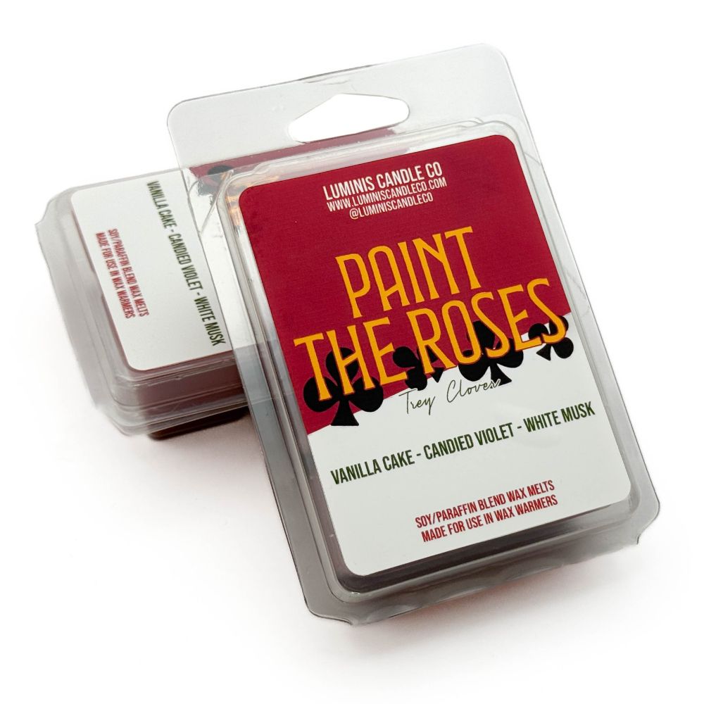 A wax melt propped up against another wax melt, both with labels that say the scent name, Paint the Roses.