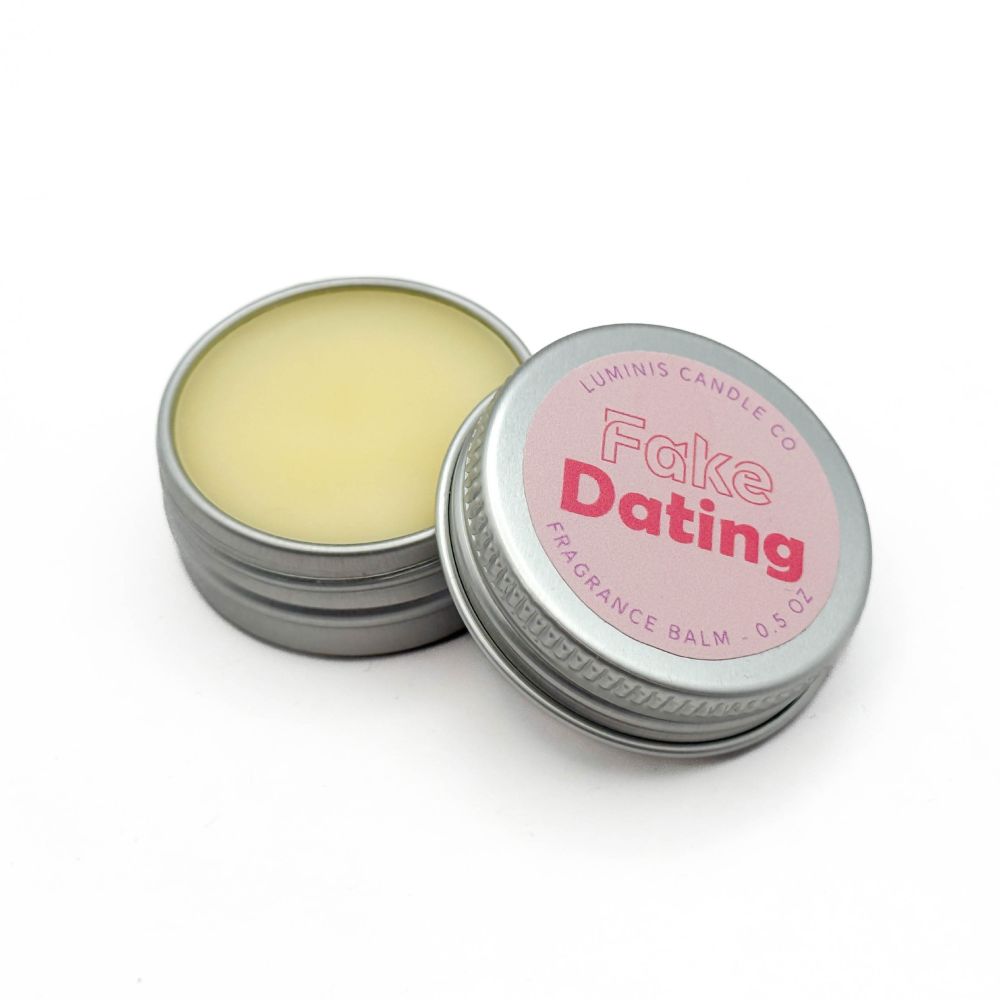 A small silver tin containing a pale yellow balm. The lid has a label that reads "Fake Dating".