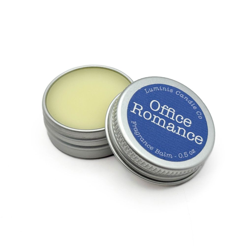 A small silver tin containing a pale yellow balm. The lid has a label that reads "Office Romance".