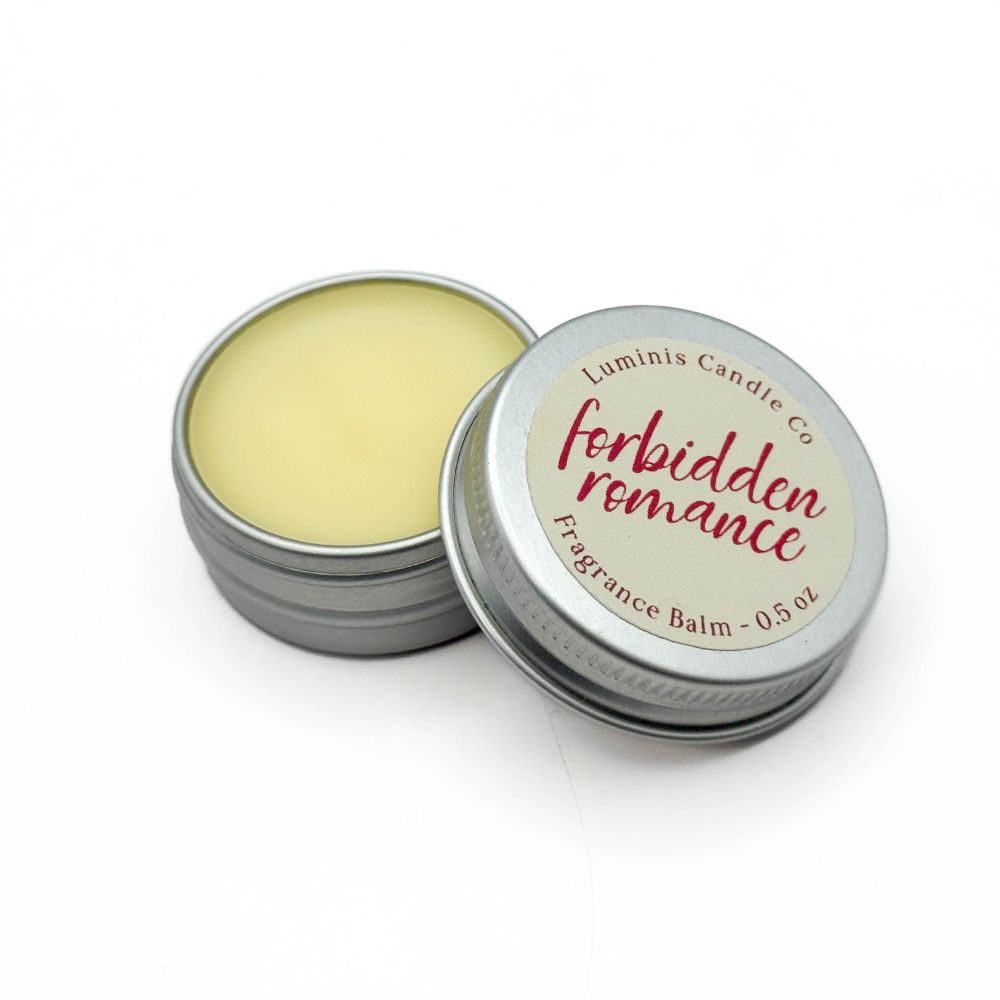 A small silver tin containing a pale yellow balm. The lid has a label that reads "Forbidden Romance".
