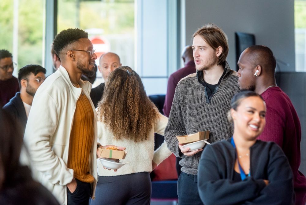 A group of people laughing and talking to each other while holding breakfast goods in a bright, light-filled space