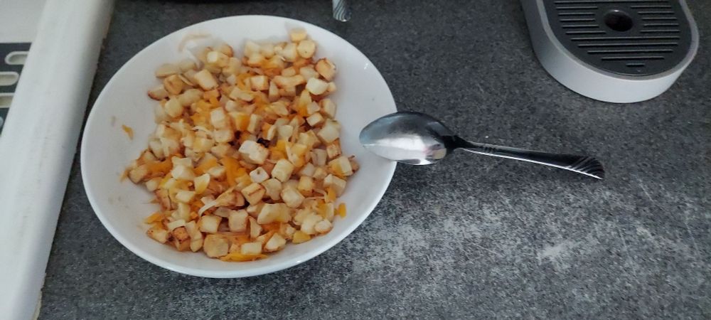 Southern-style "diced potato" hash browns covered in melted cheese in a white ceramic bowl sitting on a counter. A spoon is sitting on the edge, its other end on the counter.