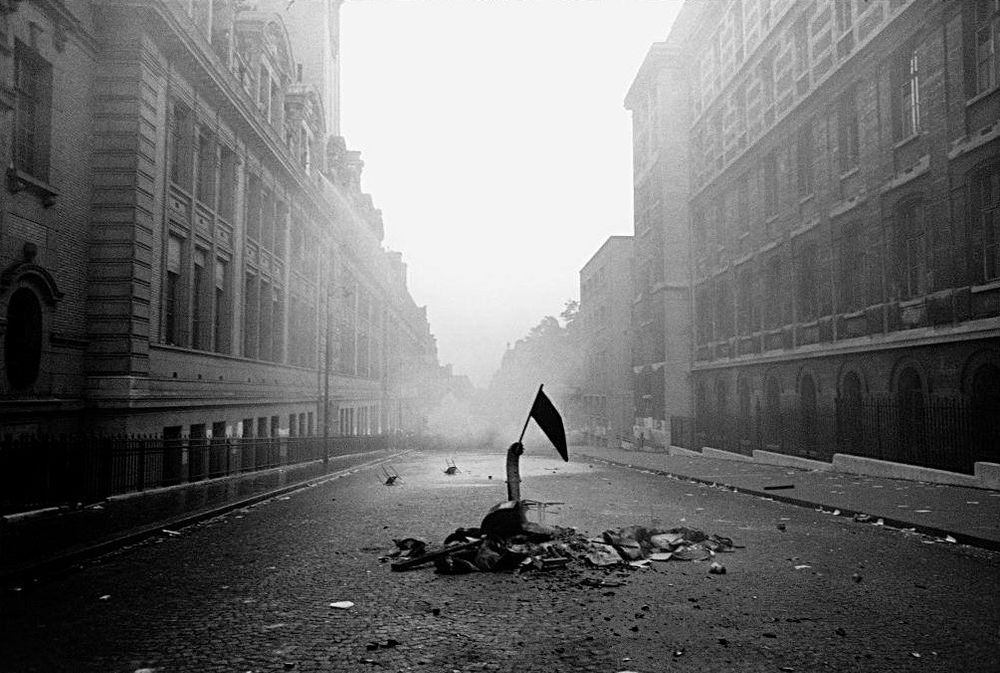 an empty street lined by tall building. detritus in the street and a flag at street level hanging limply