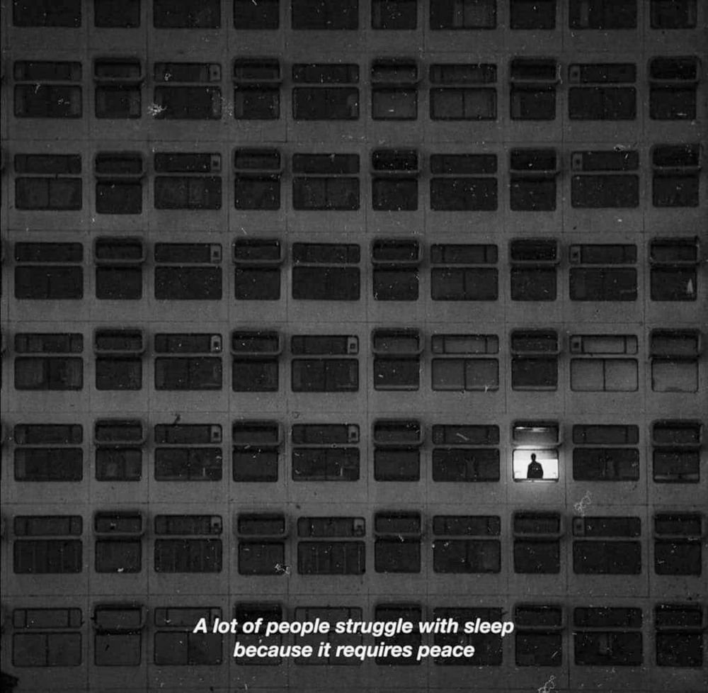 a large apartment building with a single window illuminated. a figure stood in that window.
A lot of people struggle with sleep because it requires peace