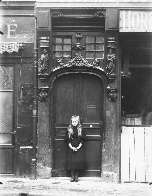 a young woman posiong infront of a door. the door is old and ornate with figures carved over the archway