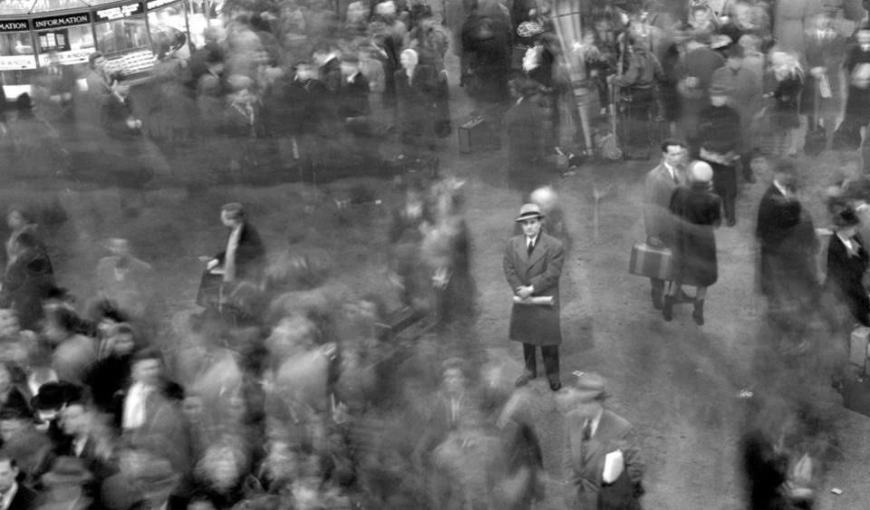 long exposure film shows a few people stood still amongst a bustling scene in a train station