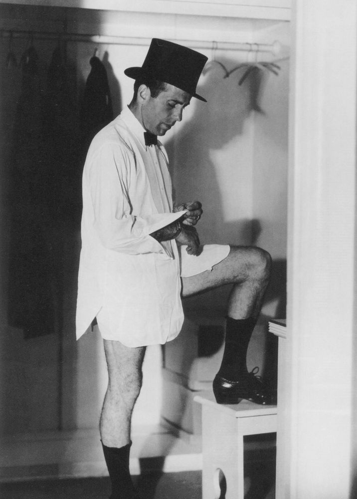 a man in a top hat, long short and no trousers, he is doing up his shirt cuff