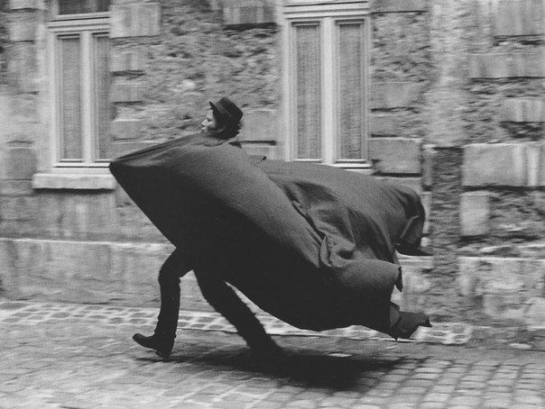 man outside, he is wearing a hat and a huge billowing cape