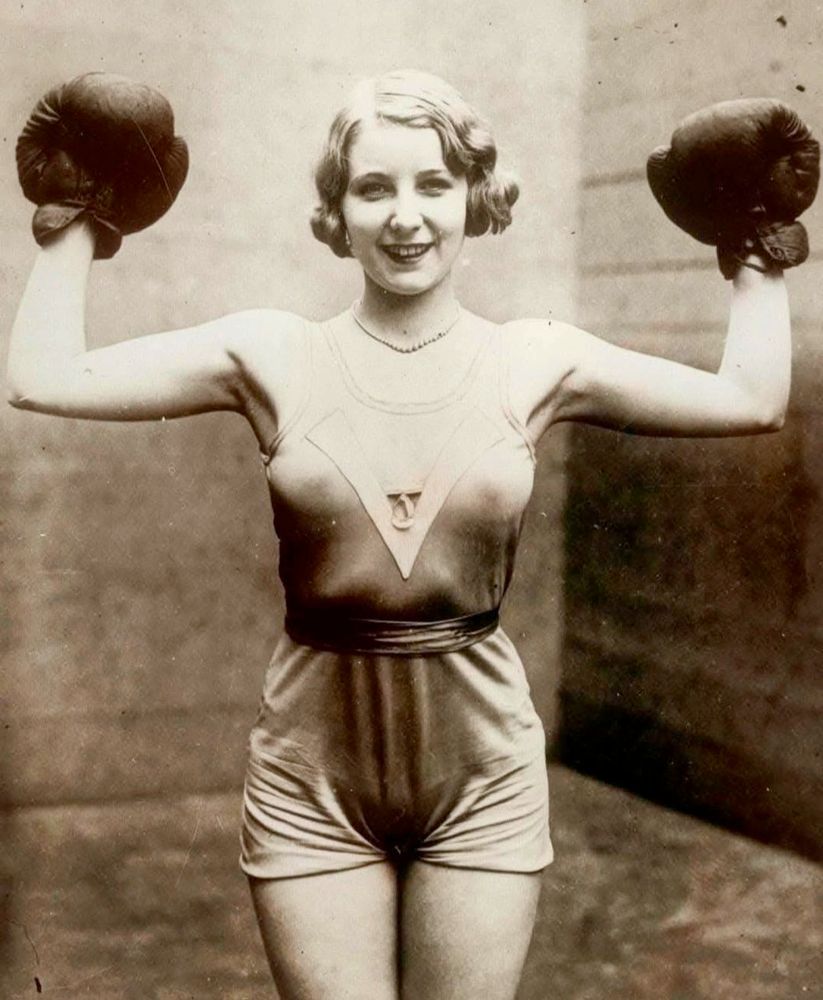 woman in gym clothes wearing boxing gloves. she is smiling