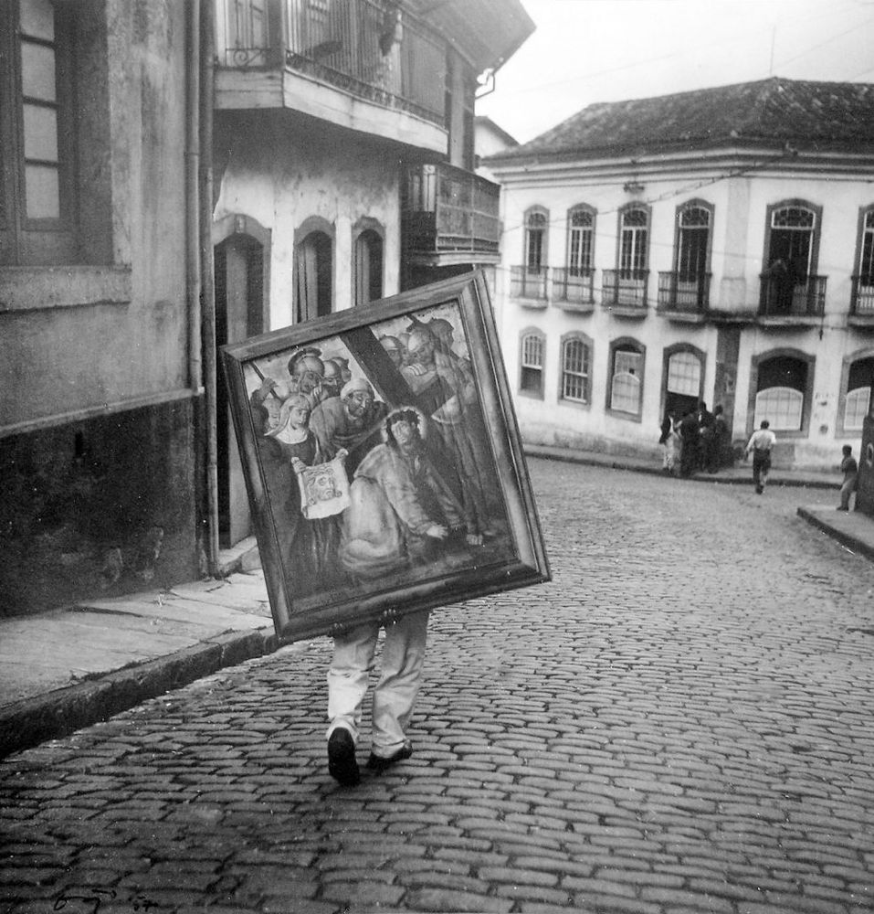 a man carrying a large painting on his back down a cobbled street