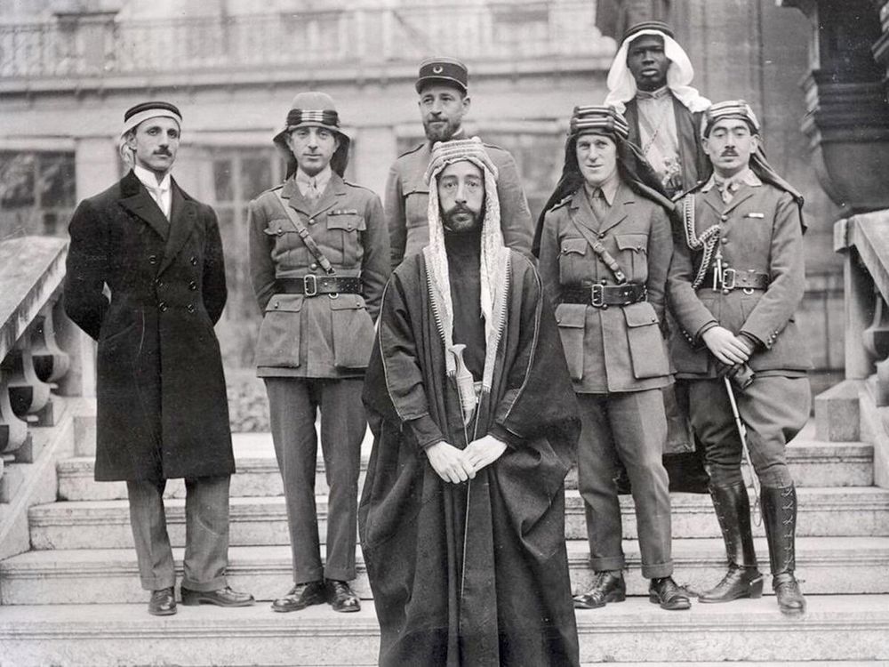 a group of men, some in uniform others in arab dress. They are stood on the steps of a building