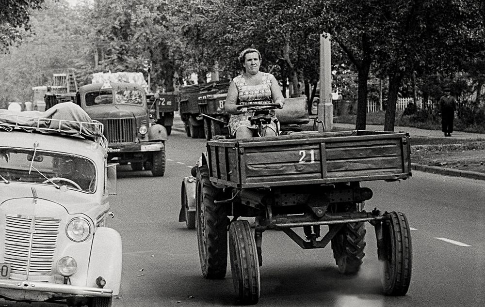 a woman driving  flatbed tractor in busy sity traffice
