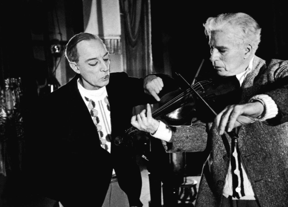 two men, one holding a violin, the other pointing at a string