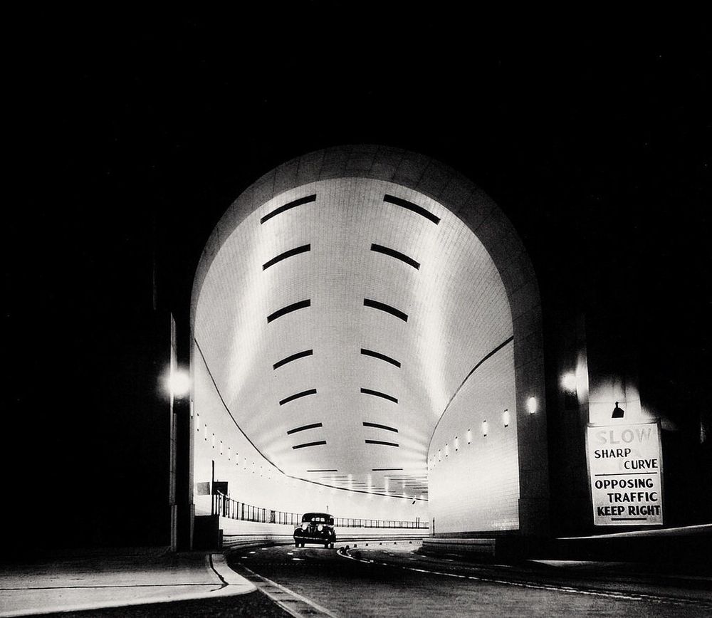 night shot of a car emerging from a large and brightly lit tunnel