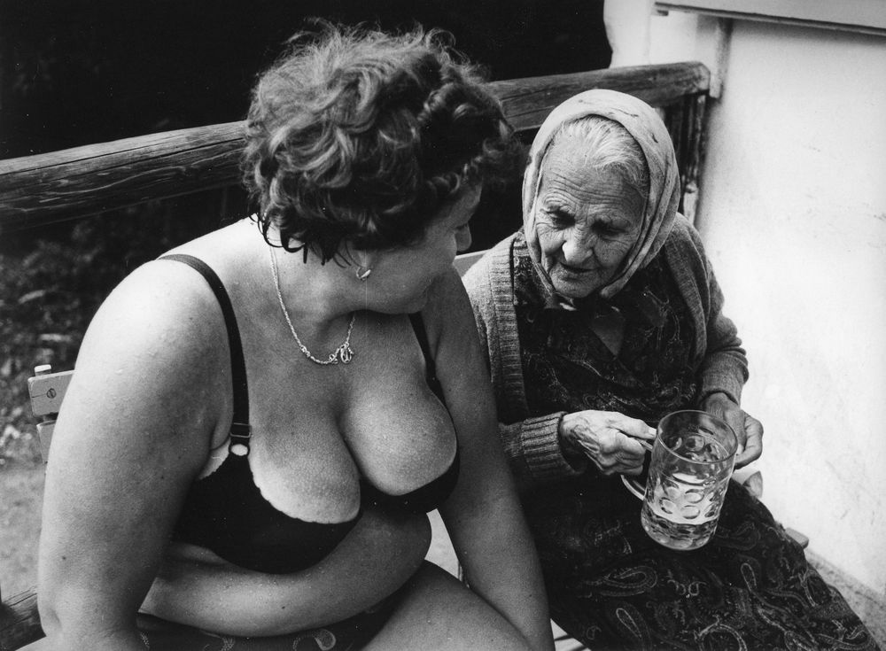 two women, one in an bikini, the other, older, holding abeer glass appears to be looking at the others breasts