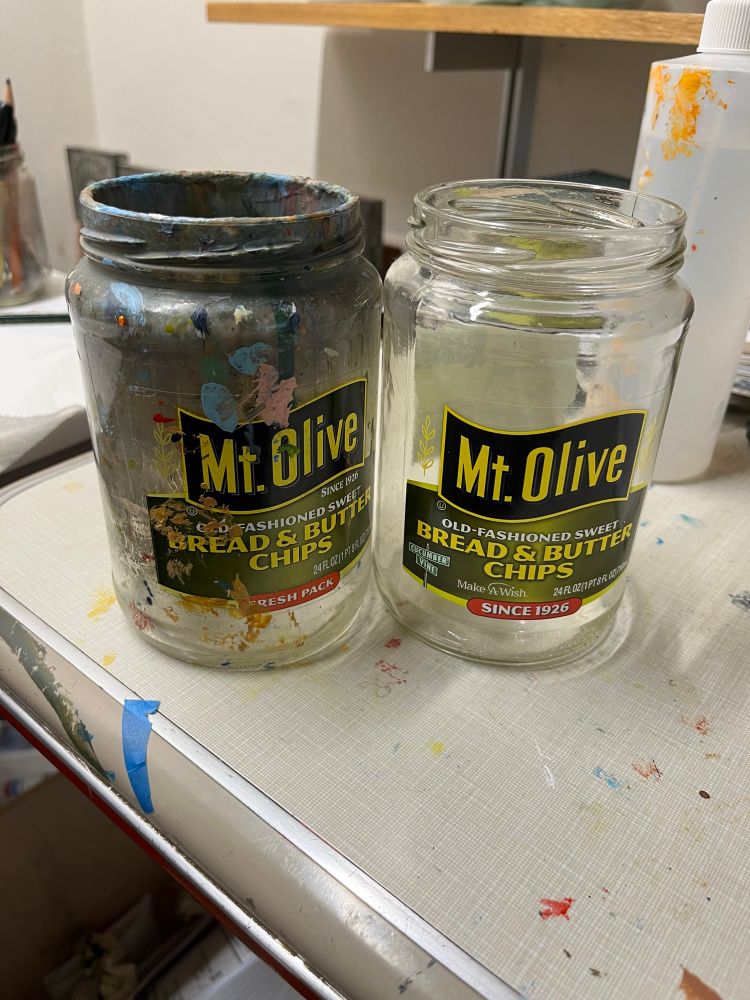 Photo of a brand new clean empty pickle jar next to the paint-encrusted one I’ve been using for about a decade. 