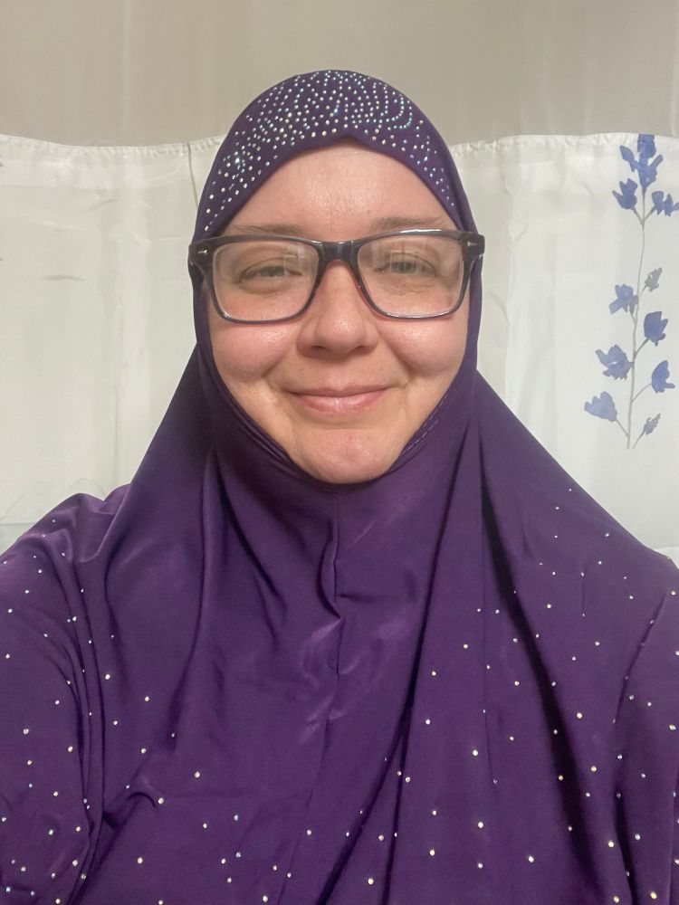 Vianna in a purple rhinestone covered hijab and purple glasses smiles in front of a white and floral curtain 