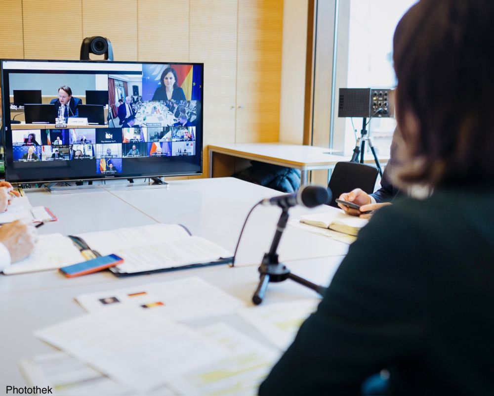 Ein Bildschirm, auf dem eine Videokonferenz mit den Kacheln der Teilnehmenden zu sehen ist. Davor Annalena Baerbock, die in ein Mikrofon spricht.