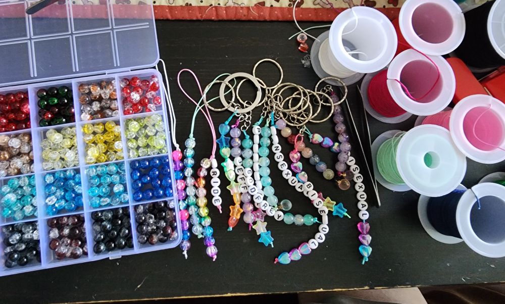 A table with craft supplies, like beads and string, and a bunch of colourful key and phone charms. 