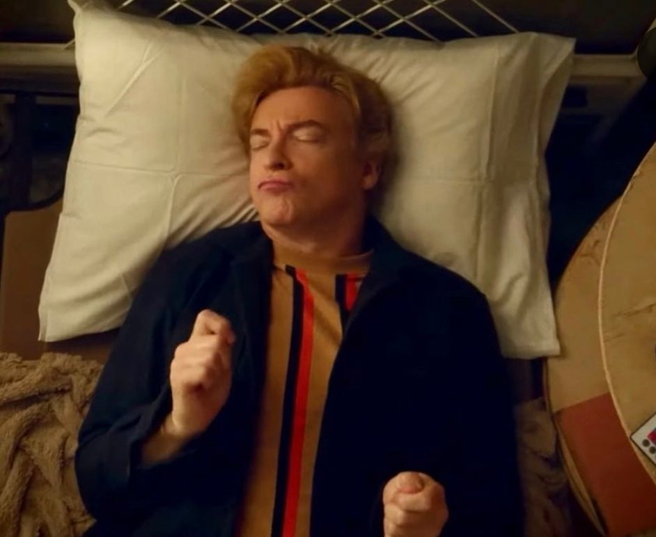 Casper, lying on a bed, eyes closed, lips pursed and his hands lookike he's in the middle of performing air drums. 