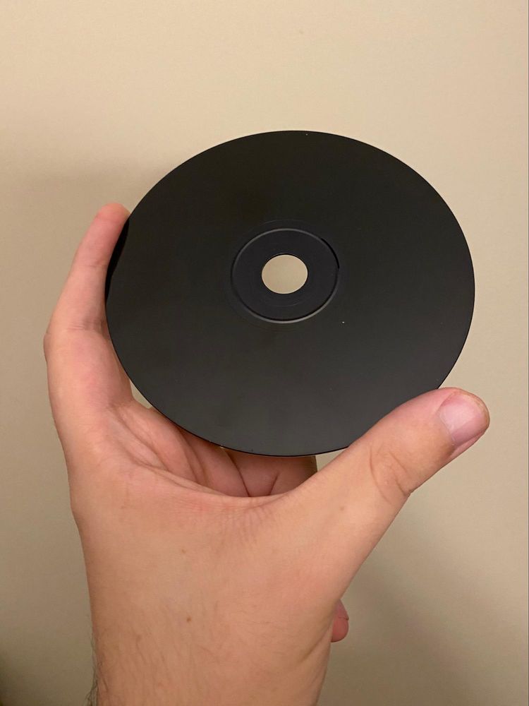Photograph of a hand holding up a black PlayStation disc.