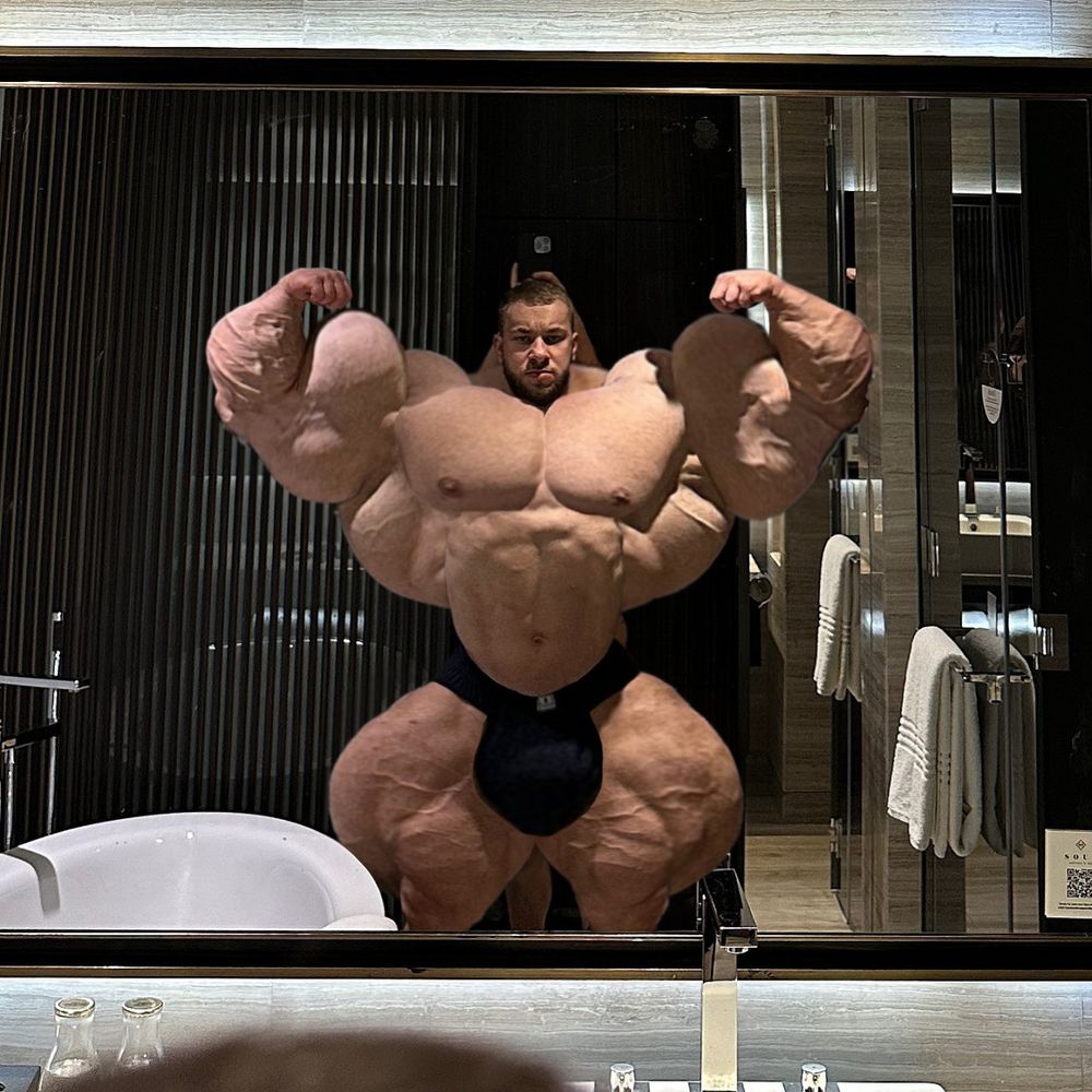 A bodybuilder posing in front of a bathroom mirror. His muscles have been photoshopped to be incredibly large. there is a person behind him holding a phone above his head to take a picture, but he is so large that the other figure is completely obscured