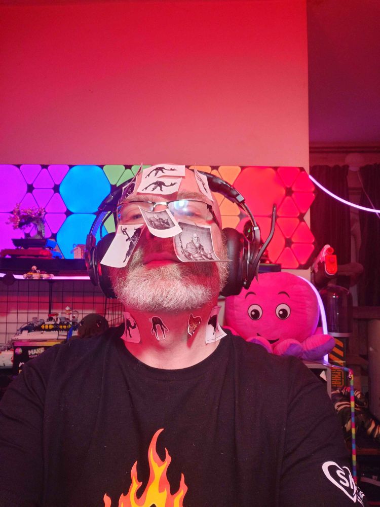 A bearded man wearing headphones with many stickers stuck to his forehead, cheeks, nose and neck.
