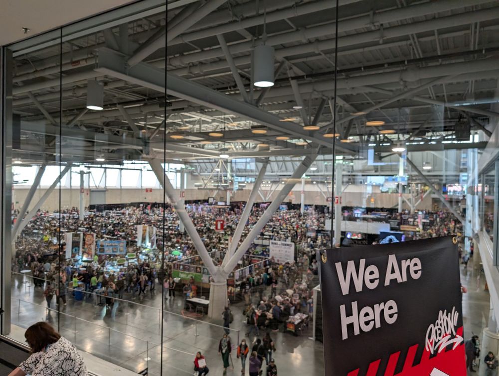 A second floor view of the Tabletop Hall at PAX East 2025. Thousands of players in seats or shopping at booths.
