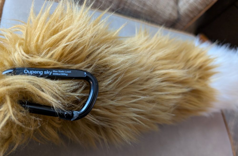 furry yellow mongoose tail with a black carribiner attached that says "Oupeng sky Max Static Load: 855lbs / 388kg"