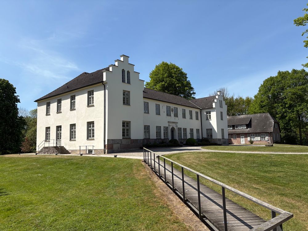 Gut Siggen der Alfred Toepfer Stiftung. Grüner Rasen vor weißem, großen Gebäude unter blauem Himmel 