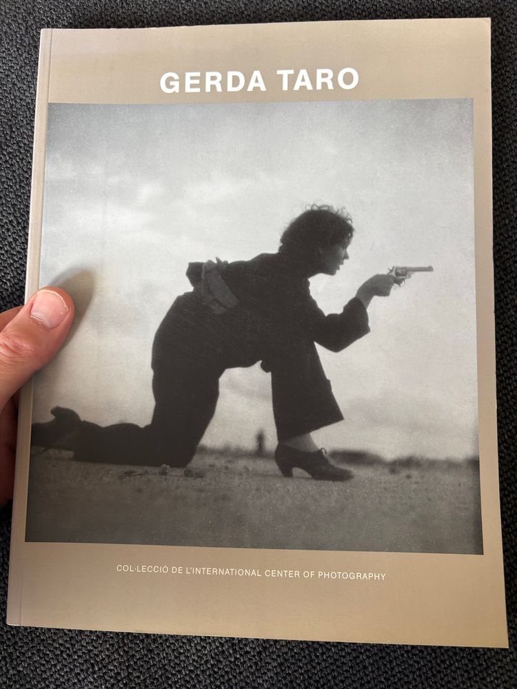 Frau kniet auf einem Bein und stützt einen Arm auf dem andern Knie ab. Hält in der Hand dieses Arms eine Pistole. Zielt. 
Cover eines Ausstellungskatalogs zu Gerda Taro aus dem MNAC in Barcelona. 